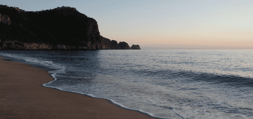 Plage sereine au coucher du soleil, falaise en arrière-plan.