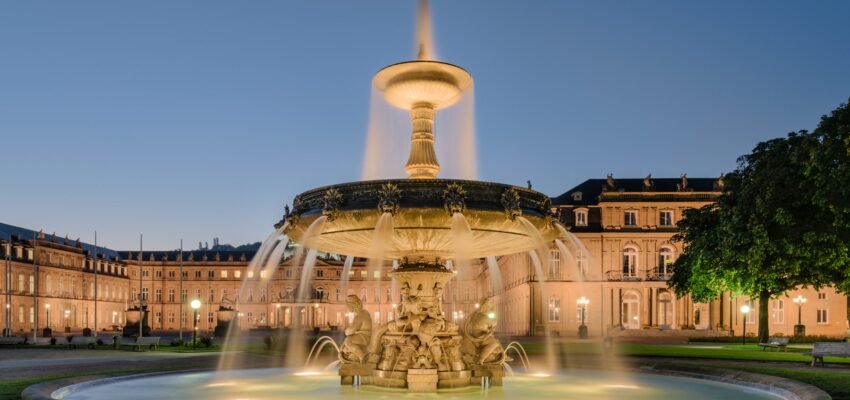 Fontaine éclairée devant bâtiment majestueux au crépuscule.